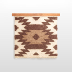 The Zytia (Life) Wool Wall Hanging, handcrafted from Carpathian wool, displays brown and cream geometric patterns on a wooden rod, honoring Ukrainian heritage on a crisp white backdrop.