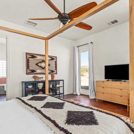 Bedroom with a ceiling fan, bed, dresser, TV, wall art, and the Myr (Peace) Wool Wall Hanging inspired by Ukraine traditional design, plus a glass door offering a view outside.