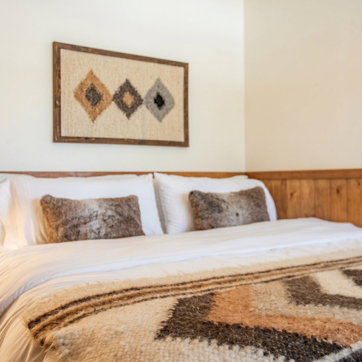 A cozy bed with furry pillows, a patterned blanket, and geometric wall art above a wooden headboard is complemented by the Harny (Beautiful) Wool Framed Wall Art for extra warmth and texture.