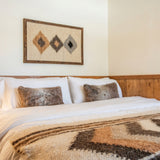 A cozy bed with furry pillows, a patterned blanket, and geometric wall art above a wooden headboard is complemented by the Harny (Beautiful) Wool Framed Wall Art for extra warmth and texture.