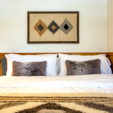 Cozy bed with two gray pillows, featuring the Harny (Beautiful) Wool Framed Wall Art with abstract diamond patterns hanging above the headboard.