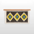 The Mriya (Dream) Wool Wall Hanging, handwoven from Carpathian wool, showcases yellow, blue, and white diamond patterns on a wooden rod—an ideal sustainable home decor piece.