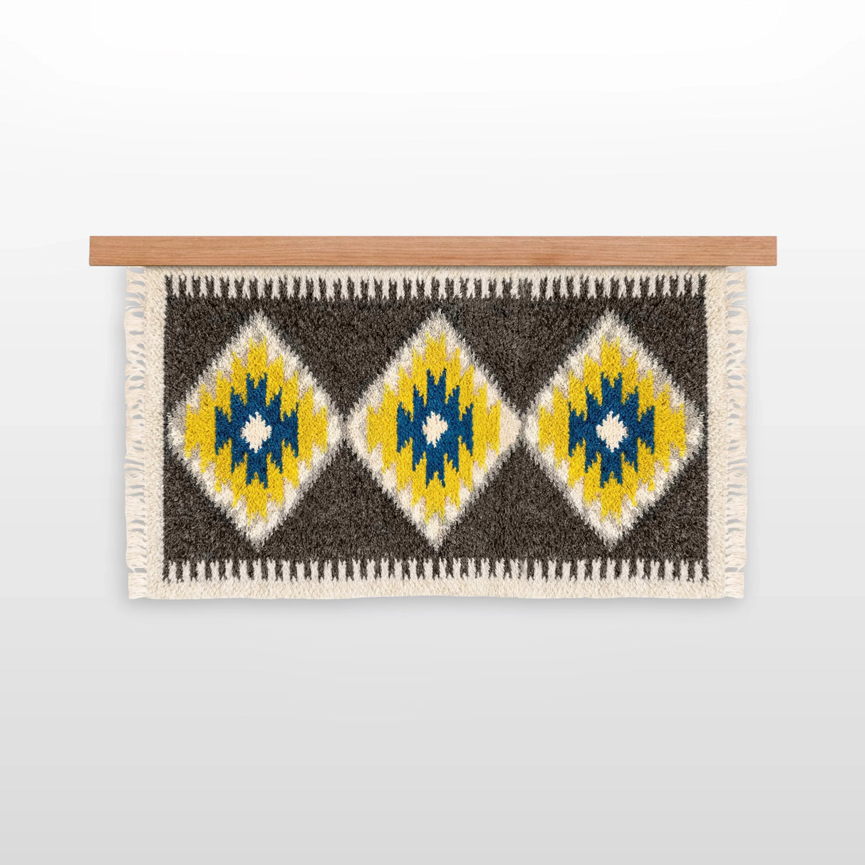 The Mriya (Dream) Wool Wall Hanging, handwoven from Carpathian wool, showcases yellow, blue, and white diamond patterns on a wooden rod—an ideal sustainable home decor piece.