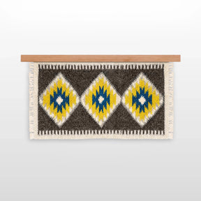 The Mriya (Dream) Wool Wall Hanging, handwoven from Carpathian wool, showcases yellow, blue, and white diamond patterns on a wooden rod—an ideal sustainable home decor piece.