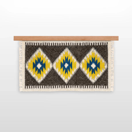 The Mriya (Dream) Wool Wall Hanging, handwoven from Carpathian wool, showcases yellow, blue, and white diamond patterns on a wooden rod—an ideal sustainable home decor piece.