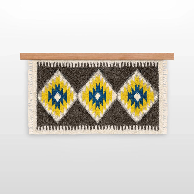 The Mriya (Dream) Wool Wall Hanging, handwoven from Carpathian wool, showcases yellow, blue, and white diamond patterns on a wooden rod—an ideal sustainable home decor piece.