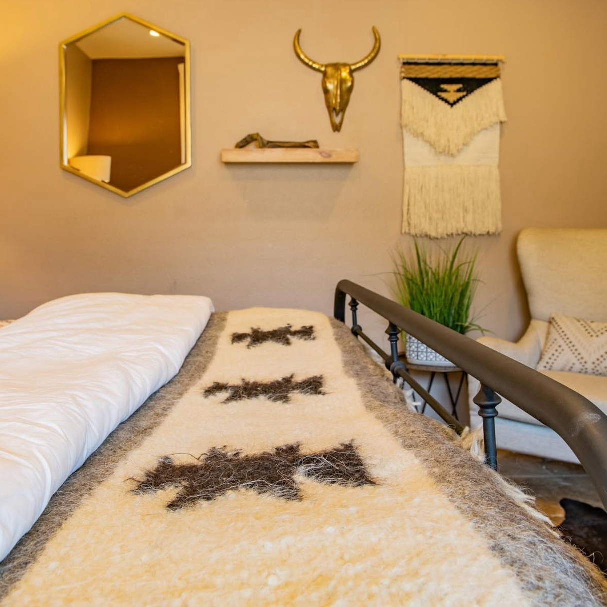 A cozy bedroom with a Chysto (Pure) Wool Statement Bed Blanket featuring traditional Ukrainian star symbols, a metal bed frame, wall decor, and a plant on a shelf.