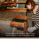 A woman weaves the Khmara (Cloud) Wool Statement Bed Blanket on a loom, highlighting traditional craftsmanship in a workshop setting.