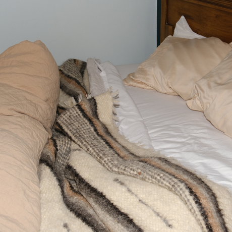Unmade bed with beige pillows and a Gratsia (Grace) Wool Statement Bed Blanket lying on white sheets, creating a cozy and stylish look.