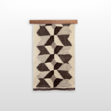 The Remeslo (Craft) Wool Wall Hanging showcases handwoven geometric brown and beige patterns made from organic wool, displayed on a wooden rod against a white background.