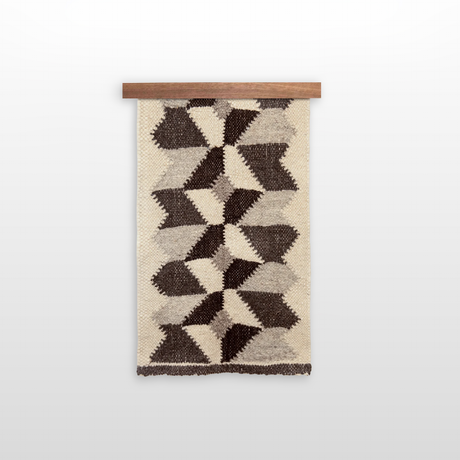 The Remeslo (Craft) Wool Wall Hanging showcases handwoven geometric brown and beige patterns made from organic wool, displayed on a wooden rod against a white background.