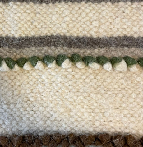 Close-up of the Faino (Fine) Wool Statement Bed Blanket, featuring white, green, brown, and gray yarn in textured horizontal stripes—a handcrafted piece that brings artisanal charm to any room.