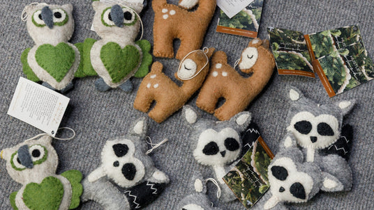 Handmade felt animal ornaments, including owls, raccoons, and deer, displayed on a gray textured surface.