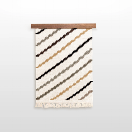 The Promin (Beam) Wool Rug / Wall Hanging, featuring diagonal brown, tan, and black stripes with fringe, comes with a Wood Rug Hanger ($240 value)—a distinctive gallery wall art piece for your space.