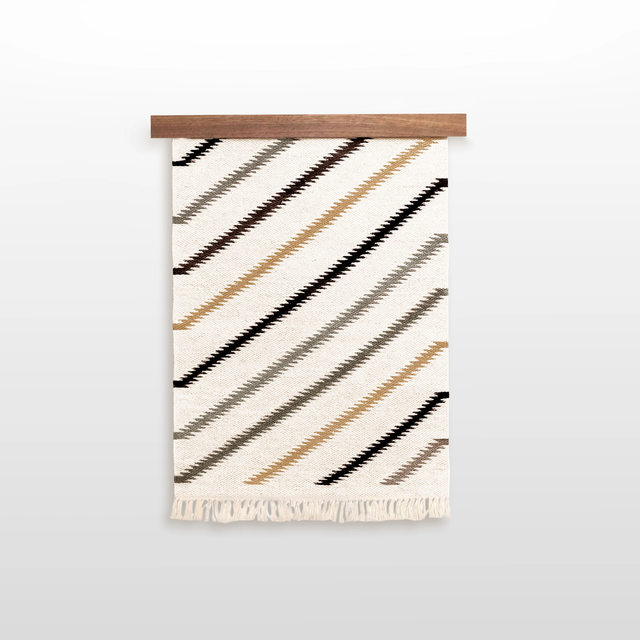 The Promin (Beam) Wool Rug / Wall Hanging, featuring diagonal brown, tan, and black stripes with fringe, comes with a Wood Rug Hanger ($240 value)—a distinctive gallery wall art piece for your space.