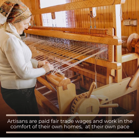 A woman weaves a Gratsia (Grace) Wool Statement Bed Blanket on a wooden loom in her home, smiling warmly as she works.