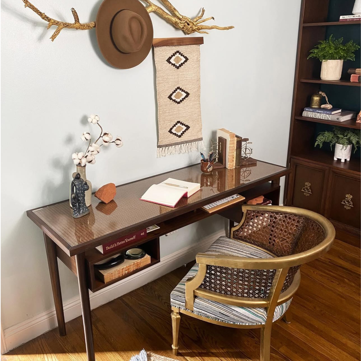 A stylish home office featuring a brown desk, gold-accented chair, books, and wall decor on hardwood floors, completed by the Heredij (Heritage) Wool Rug / Wall Hanging, which brings intricate design and rich texture to the space.