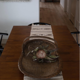A wicker basket with a flower sits on a Wool Table Runner atop a wooden dining table with black chairs.