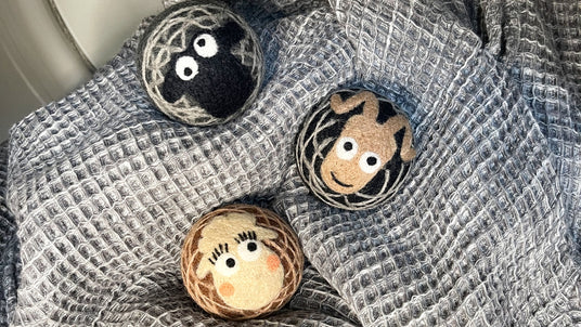 Three round felted balls with animal and face designs resting on a textured gray fabric.