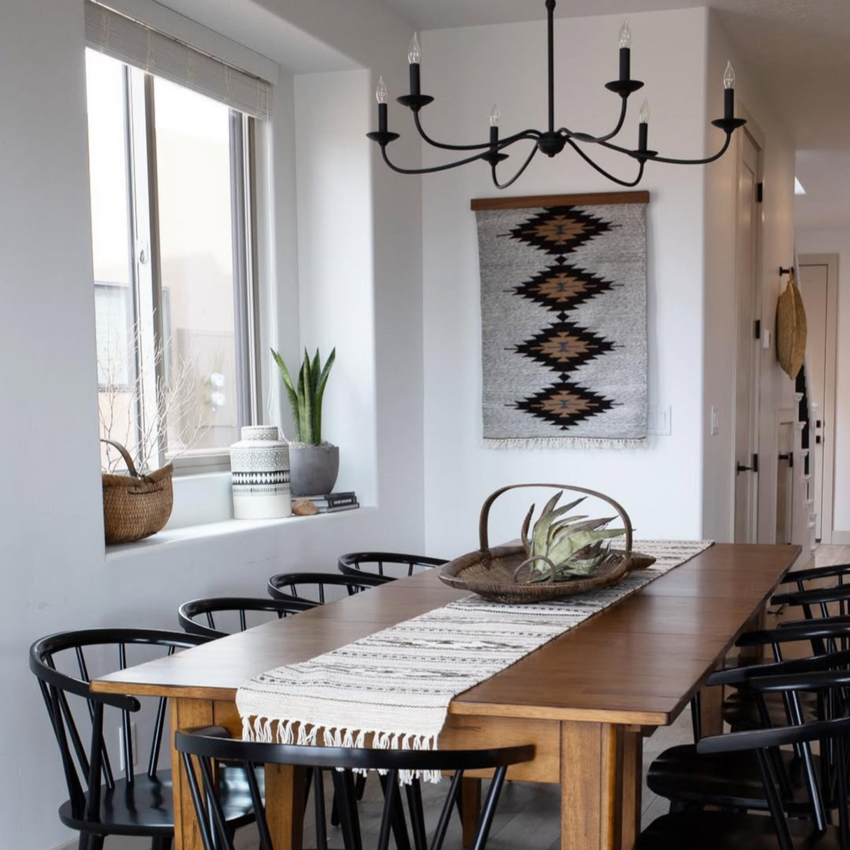 Modern dining room with a wooden table, black chairs, plants, and the Smilyv (Bold) Wool Rug underfoot and as a woven wall hanging above the table.