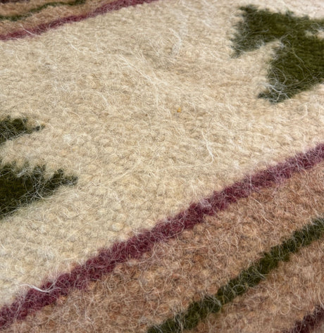 Close-up of the Sosna (Pine) Wool Statement Bed Blanket—handwoven from Carpathian sheep wool, showcasing green and brown geometric patterns on a cream background.