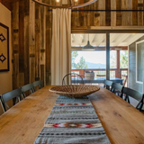 Rustic dining room with a wooden table featuring a Wool Table Runner, black chairs, a woven basket, and a mountain view through glass doors.