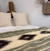 Neutral pillows and a woven basket above a cozy bed with the Handmade in Ukraine, Organic Natural 100% Sheep Wool Woven Statement Blanket Bed Covering Bedspread Duvet in green and cream patterns.