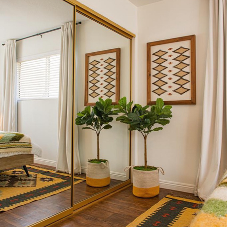 A Blazheny (Blissful) Wool Rug adds warmth by mirrored closet doors in a cozy bedroom with patterned decor and wooden floors, perfectly complementing the room’s inviting, stylish neutral interior design.