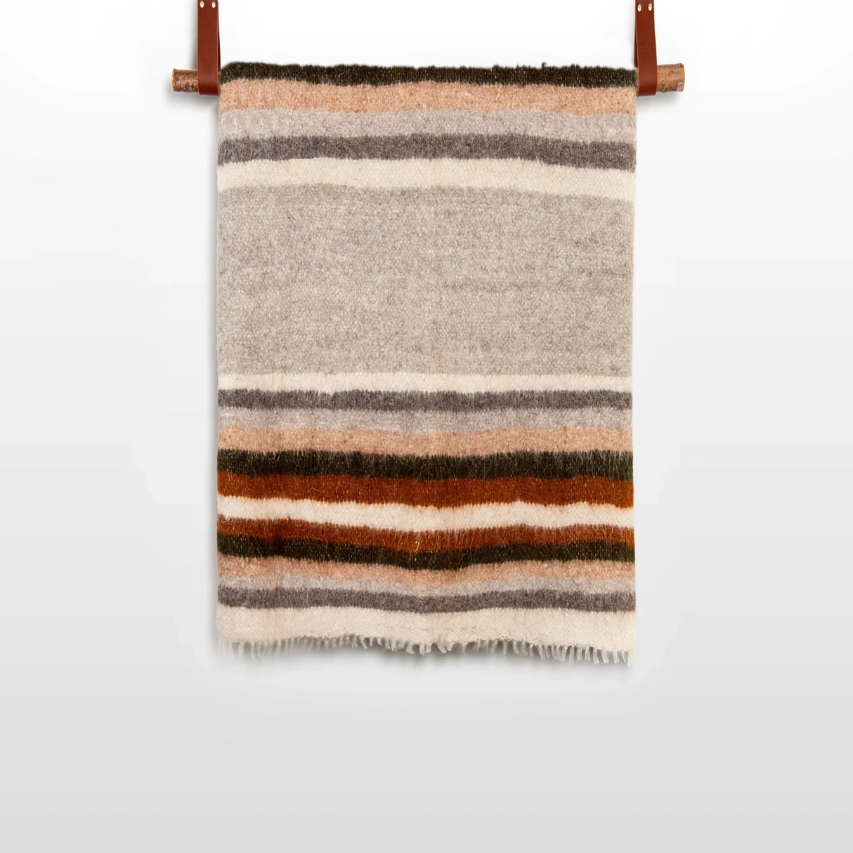 The Mudry (Wise) Wool Statement Baby Blanket, handwoven from organic Carpathian wool with horizontal brown, orange, gray, and beige stripes, hangs on a rod.