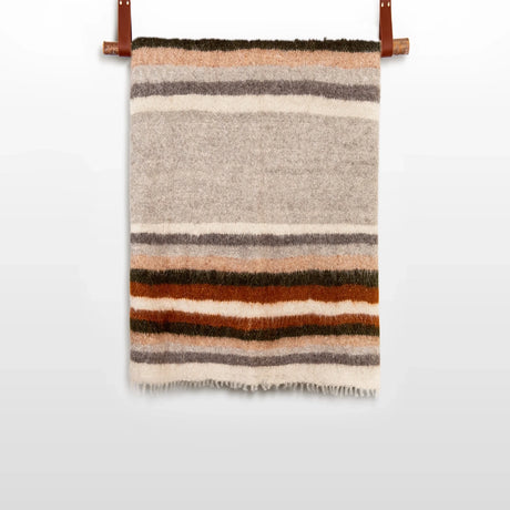 The Mudry (Wise) Wool Statement Baby Blanket, handwoven from organic Carpathian wool with horizontal brown, orange, gray, and beige stripes, hangs on a rod.