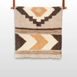 The Myr (Peace) Wool Statement Bed Blanket, crafted from organic Carpathian wool, features a beige and brown geometric pattern and hangs elegantly on a wooden rod.
