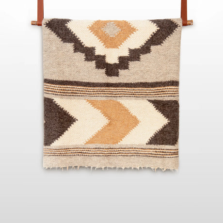 The Myr (Peace) Wool Statement Bed Blanket, crafted from organic Carpathian wool, features a beige and brown geometric pattern and hangs elegantly on a wooden rod.