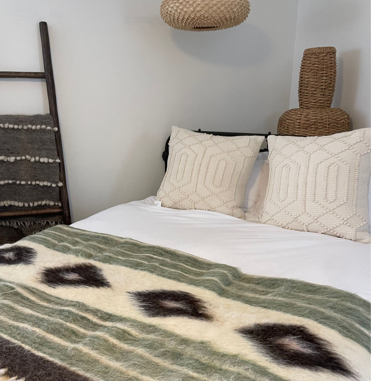 A cozy bed with patterned pillows is topped with a Handmade in Ukraine, Organic Natural 100% Sheep Wool Woven Statement Blanket Bed Covering Bedspread Duvet, adding warmth to this modern, boho-style bedroom.