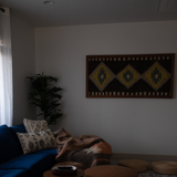 Cozy living room with a blue sofa, patterned pillows, throw blanket, plant, geometric wall art, and the Mriya (Dream) Wool Wall Hanging handcrafted from Carpathian sheep wool.