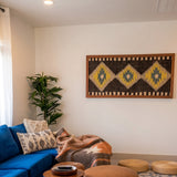 Cozy living room with blue sofa, patterned cushions, wall art, plant, woven poufs, and the Mriya (Dream) Wool Wall Hanging for sustainable home decor.
