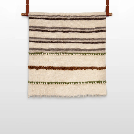 The Faino (Fine) Wool Statement Bed Blanket features horizontal stripes in brown, green, and cream, crafted to resemble a handwoven textile and accented with two leather straps for hanging.