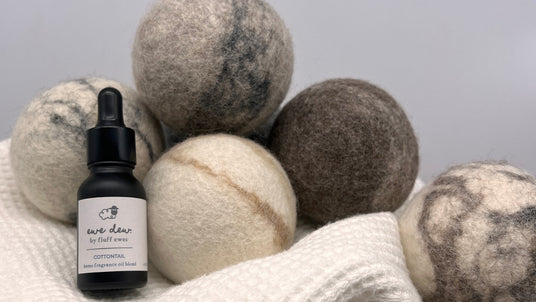 A dropper bottle and five wool dryer balls rest on a textured white cloth against a plain background.