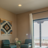 Two chairs and a small table with a plant by a window, featuring the Zirka (Star) Wool Wall Hanging and curtains, with outdoor views.