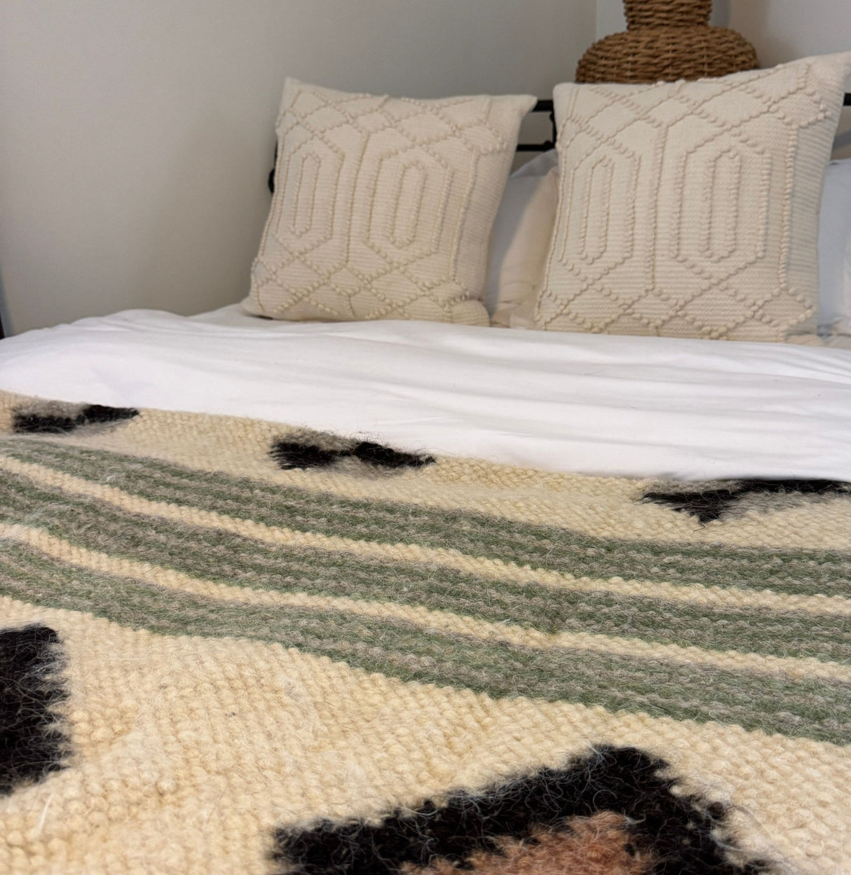 A bed with two textured cream pillows and a Handmade in Ukraine Organic 100% Sheep Wool Woven Statement Blanket, featuring green and black accents, adds warmth and charm.