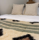 A bed with two textured cream pillows and a Handmade in Ukraine Organic 100% Sheep Wool Woven Statement Blanket, featuring green and black accents, adds warmth and charm.