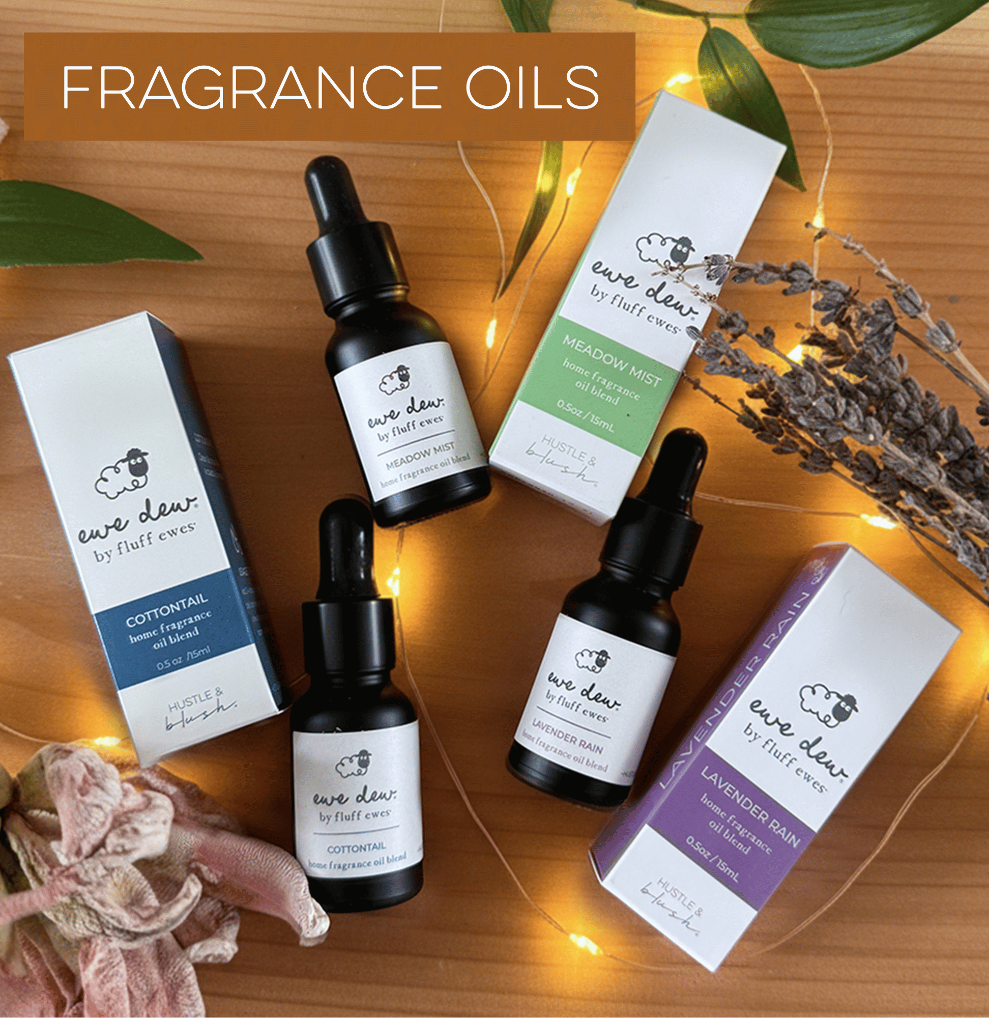 Three bottles of Eve Dew fragrance oils with boxes, dried flowers, and string lights on a wooden surface.