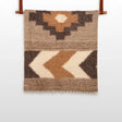 The Myr (Peace) Wool Statement Bed Blanket features geometric patterns in brown, beige, and cream on a white background, crafted from organic wool for a cozy, natural touch.