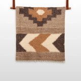 The Myr (Peace) Wool Statement Bed Blanket features geometric patterns in brown, beige, and cream on a white background, crafted from organic wool for a cozy, natural touch.