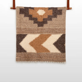 The Myr (Peace) Wool Statement Bed Blanket features geometric patterns in brown, beige, and cream on a white background, crafted from organic wool for a cozy, natural touch.