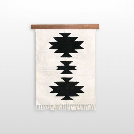 The Chysto (Pure) Wool Rug / Wall Hanging features black geometric patterns on white, inspired by Ukrainian weaving heritage. Includes wood rug hanger ($240 value). Finished with fringe at the bottom.