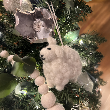 An 8' hand-felted natural cream organic wool garland hangs on a decorated Christmas tree with green branches and white lights.
