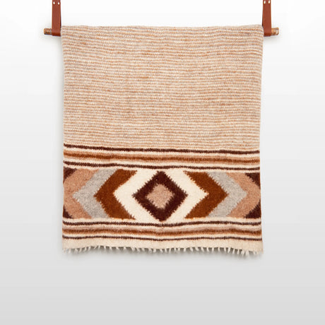 The Tkach (Weaver) Wool Statement Bed Blanket features tan and brown stripes with geometric diamond patterns, handwoven in wool and displayed on a leather strap.