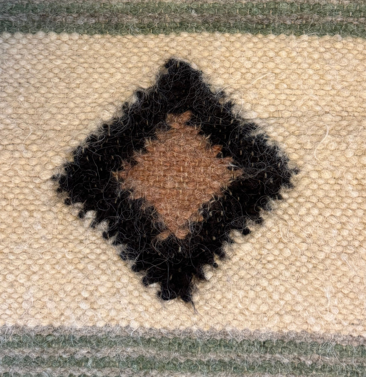 Handmade in Ukraine, this organic 100% sheep wool blanket features a central brown diamond bordered by black on a cream background with green stripes—a striking woven statement bedspread and bed covering.