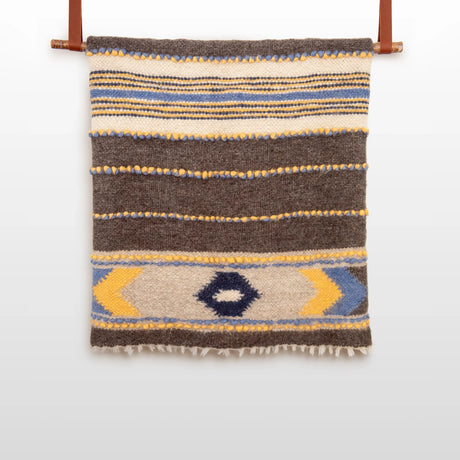 The Zoloty (Golden) Wool Statement Bed Blanket features geometric patterns in brown, white, yellow, and blue, inspired by Ukrainian artisan designs.