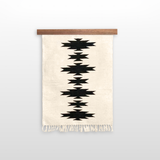 The Chysto (Pure) Wool Rug / Wall Hanging, handwoven from Carpathian sheep wool with black geometric patterns and fringes, comes mounted on a hemlock wood rug hanger ($240 value).